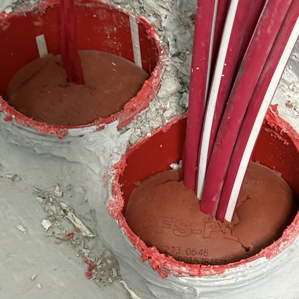 Two cored penetrations with cables through them, filled with a red firestop seal.