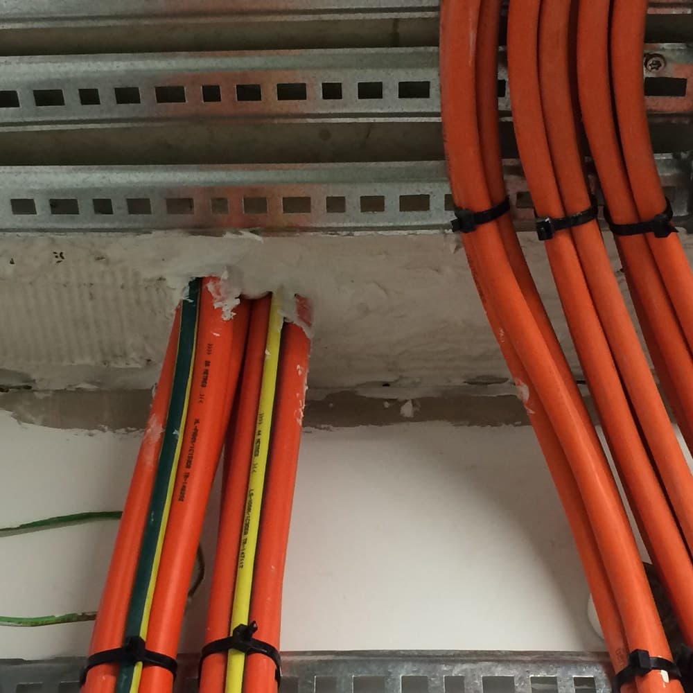 Orange electrical conduits on a cable ladder, passing through a sealed wall penetration.
