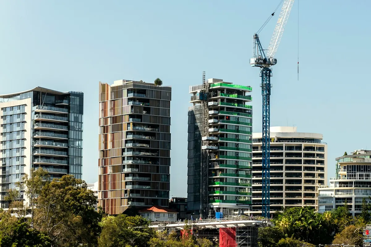 Mid-rise apartment towers beside the Brisbane River, one under construction with a tower crane
